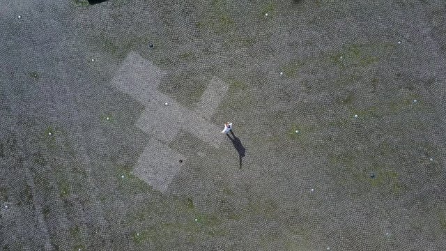 Girl standing in the middle of the square in the Alnarp university waving and a drone flying away from her showing the area around the campus.