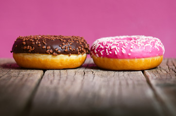 Donut with sprinkles on a wooden table and pink background. Two types of donuts. Cake and sweet. Food detail. Close up. Pastel color