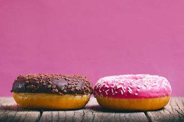 Donut with sprinkles on a wooden table and pink background. Two types of donuts. Cake and sweet. Food detail. Close up. Pastel color