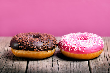 Donut with sprinkles on a wooden table and pink background. Two types of donuts. Cake and sweet. Food detail. Close up. Pastel color