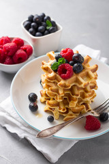 Delicious homemade waffles with fresh berries on concrete background