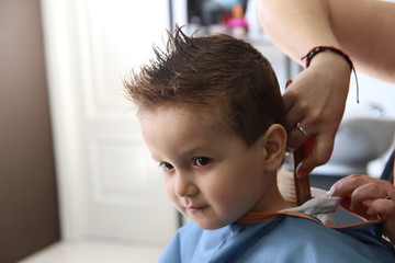ni&ntilde;o en la peluquer&iacute;a con peinado moderno y manos de peluquera cepillando pelos