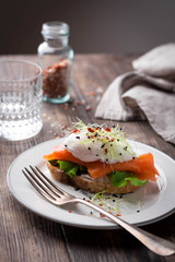 Delicious toast with salad, salted salmon and poached egg on rustic background;