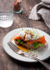 Delicious toast with salad, salted salmon and poached egg on rustic background;