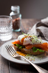 Delicious toast with salad, salted salmon and poached egg on rustic background;