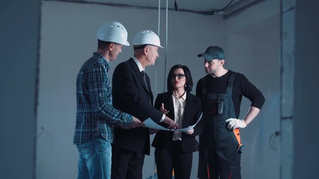 The development group of a project standing and discussing the plan on a site then turn on camera and looking straight and snile