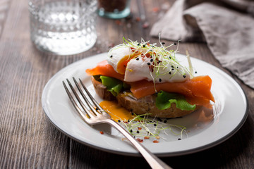 Delicious toast with salad, salted salmon and poached egg on rustic background - obrazy, fototapety, plakaty