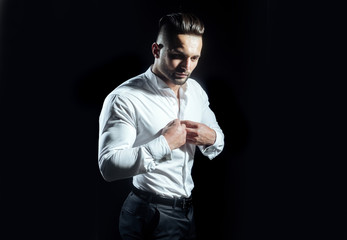 Man buttons up his white shirt standing on black background. Businessman thinks about business in...