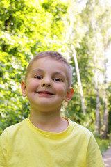 Happy child. Little boy smiles and looks directly at the camera on a background of green trees in a summer park