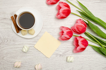 Pink tulips, blank sheet of paper, mug of coffee and marshmallows, light wooden background. top view, space for text