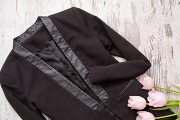 Fashionable concept. Classic black jacket and pink tulips. Top view, light wooden background