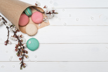 Package with colored macaroons and flowers on a white wooden background