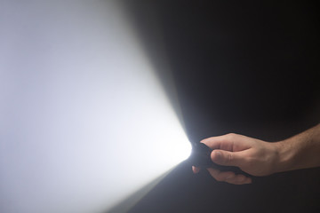 Male hand with led flashlight aimed into the frame, the light beam on black background