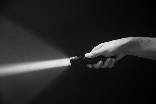 The flashlight in the man's hand from the right side of the frame in black and white color isolated on black background
