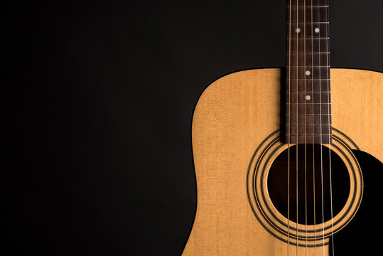 Part of a wooden acoustic guitar on the right side of the frame, on a black isolated background