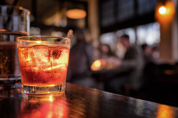 Cocktail hautnah in einer Bar-Umgebung. Verschwommene Menschen im Hintergrund. Selektiver Fokus auf das eisige Getränk und das Glas.