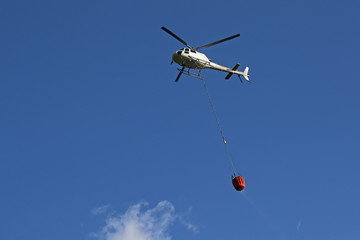 Helicopter picking up  and carrying water during fire fighting operations against blue skies
