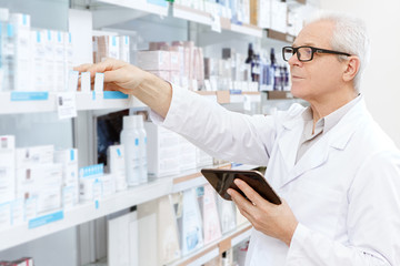 Elderly male pharmacist using digital tablet at work