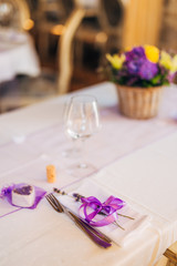 Wedding table setting at a banquet. A plate and instruments tied with a purple ribbon.