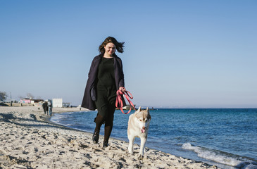 Young woman running on sea beach with siberian husky dog