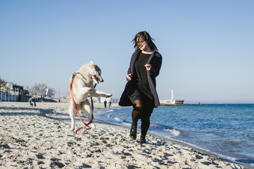 Young woman running on sea beach with siberian husky dog