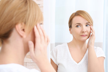 Obraz na płótnie Canvas Happy senior woman applying anti-aging cream near mirror