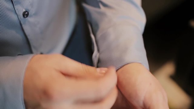Young businessman getting dressed at morning. Man buttons cuffs on shirt, putting his suit. Close-up view of male hands.
