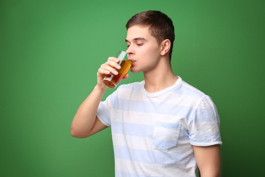 Young man drinking juice on color background