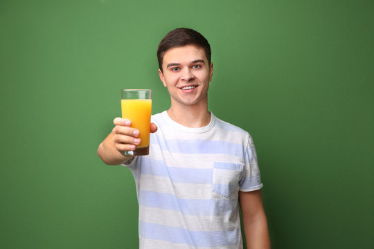 Young man drinking juice on color background