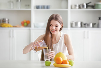 Obraz na płótnie Canvas Young woman pouring fresh juice at kitchen