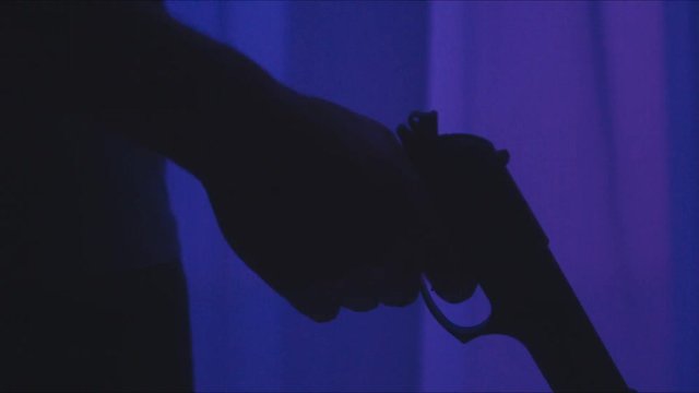 DOLLY IN Silhouette of male criminal pulling back the hammer of a pistol, police lights in the street. 4K UHD RAW edited footage
