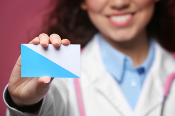 Female doctor with business card on color background, closeup