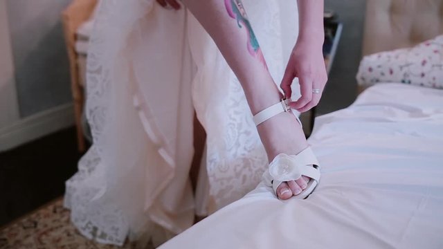 Close-up view of young bride with tattoo on the leg puts on the wedding shoes. Morning preporation before ceremony.