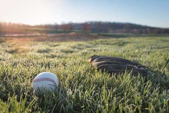 Baseball glove and ball on field in early morning grass and dew as sun rises in background