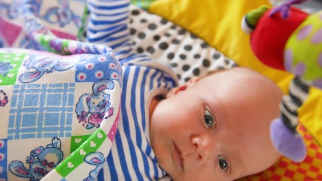 Top view shot of cute baby with soother lying in crib and looking at spinning taddy bear toys
