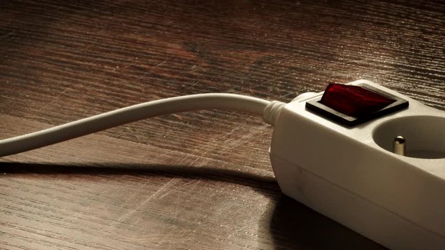 Electricity at home. Close up of white electric power strip or extension cord block for extending plug with red switch on off, on wooden floor. Dolly slider shot 4K ProRes HQ codec