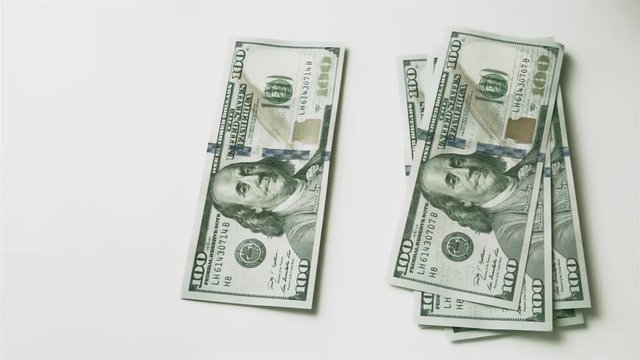 Splitting money into two unequal stacks. Men's hand puts hundred-dollar bills on the table, and then takes them away. Fast motion.