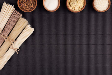 Decorative border of bundles raw noodles with ingredient in wooden bowls on black striped mat...