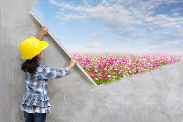 Little girl engineering ideas concept with hand holding plastering tools renovating a house. With painting flowers grass field blue sky clouds nature landscape on wall