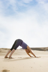 Fototapeta na wymiar Fit Lady Doing Downward Dog Yoga Pose in the Sand