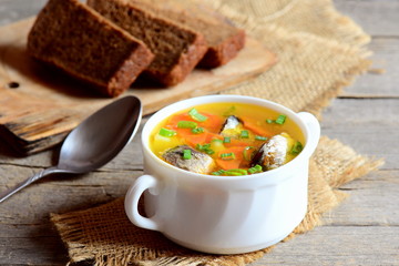 Easy fish soup recipe. Diet fish soup with potatoes, carrots and green onions in a bowl. Rye bread pieces, spoon on rustic wooden table. Closeup