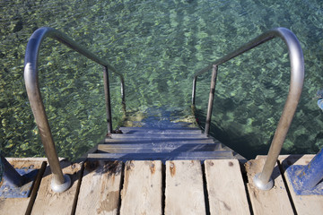 Steps with iron rails descend into clear blue water