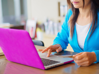 Pretty Young womans hands holding a credit card and using laptop computer for online shopping. Online payment. Female working on laptop in a cafe.