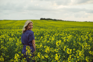 Fototapeta premium Young woman standing outdoor in rapeseed flower field and smiling