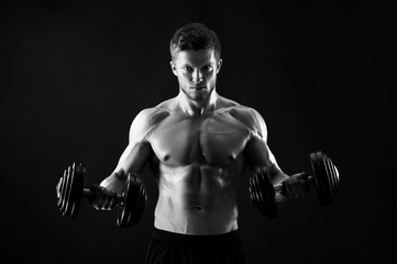 Handsome young man doing weight training with dumbbells black and white studio shot gym fitness...