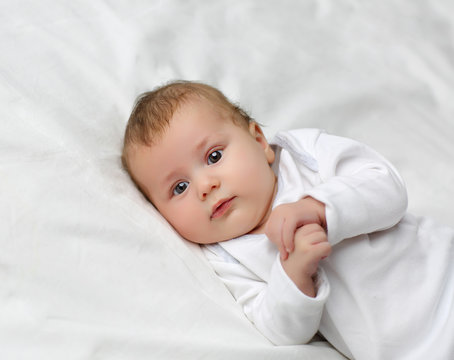 Portrait of an adorable 3 month old baby in the bedroom on the bed in white clothes