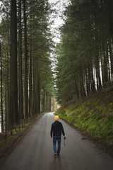 Man walking away down road between trees with camera