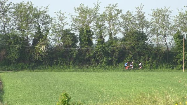 cyclists passing on horizon line of cultivated fileds