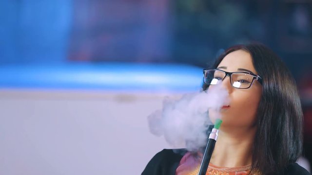 Beautiful girl smokes a hookah in a night bar