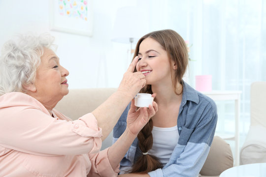 Beautiful girl and grandmother taking skin care on couch at home